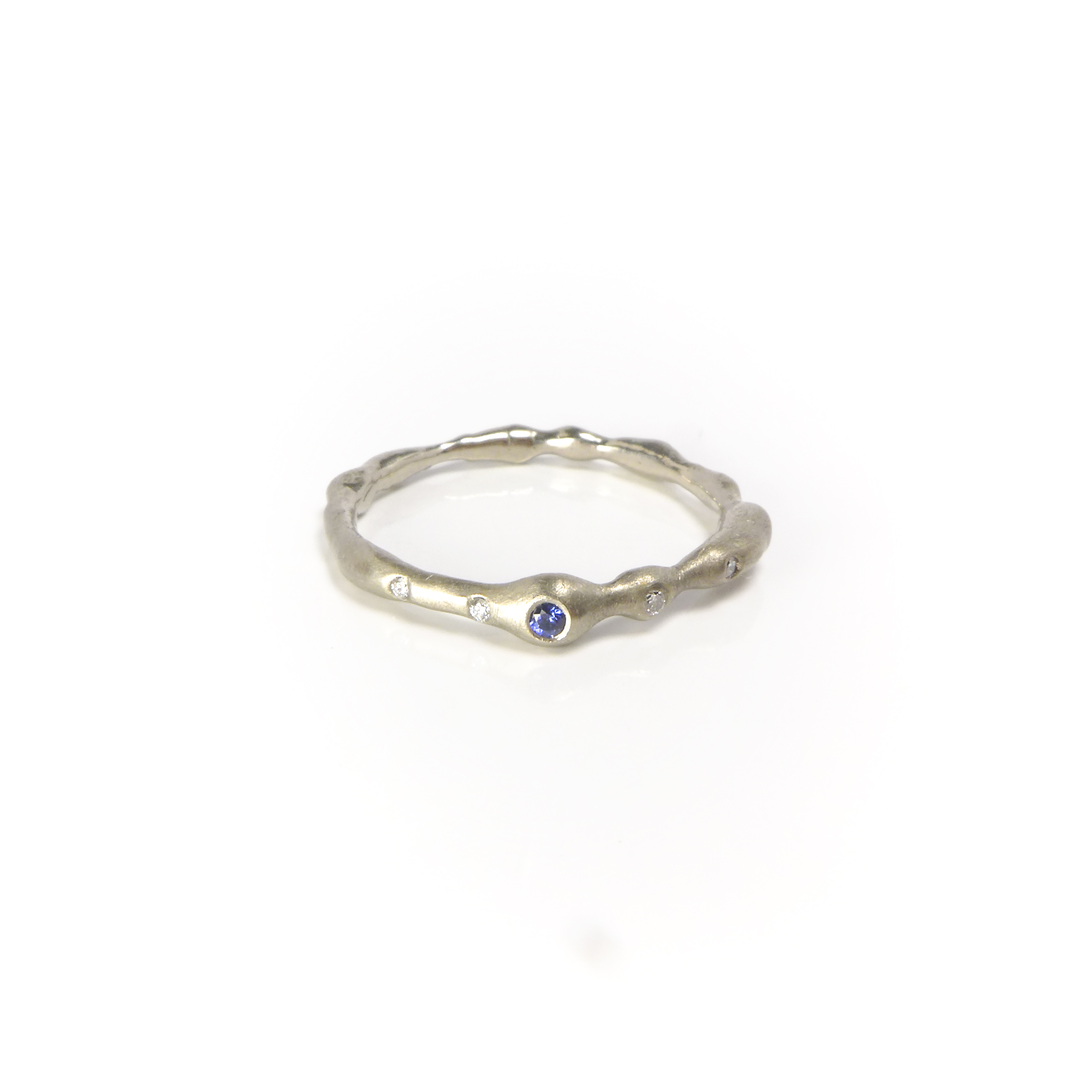 organically shaped whitegold ring with a small blue sapphire and small diamonds